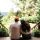 Couple sits on a wooden porch railing with their backs to the camera, looking out over a lush garden and hills beyond. An Authentic Bed and Breakfast Experience in the North Georgia Mountains