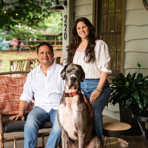 Smiling couple seated on a porch with a large gray Great Dane in front of them on a striped rug. An Authentic Bed and Breakfast Experience in the North Georgia Mountains