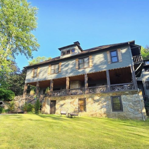 Beechwood Inn in Clayton, GA, a two-story gray house with a stone base, wooden shutters, and a large wraparound porch surrounded by trees and a grassy yard.