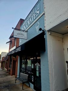 Exterior of Main Street Chocolates storefront with a blue brick facade and an ice cream cone sign; signage advertises fudge, ice cream, and coffee.