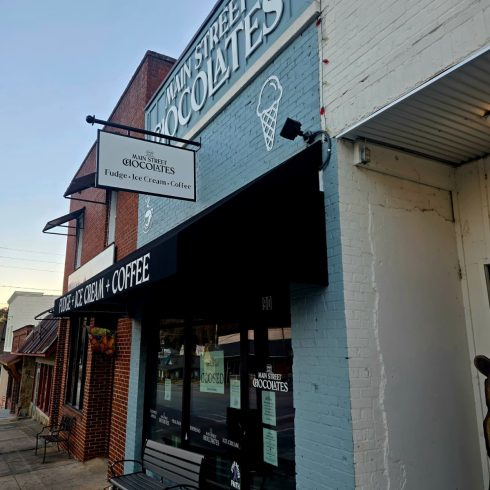 Exterior of Main Street Chocolates storefront in Clayton, GA, with a blue brick facade and an ice cream cone sign; signage advertises fudge, ice cream, and coffee.