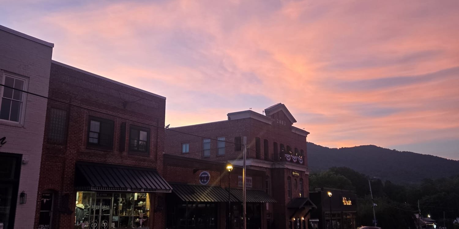 Downtown Clayton, GA street at dusk with pink and purple sky, brick buildings, and mountain silhouette in the background.