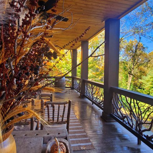 North Georgia fall getaway - Wooden porch with a trough of orange pumpkins and dried grasses, set against autumn foliage and a blue sky.