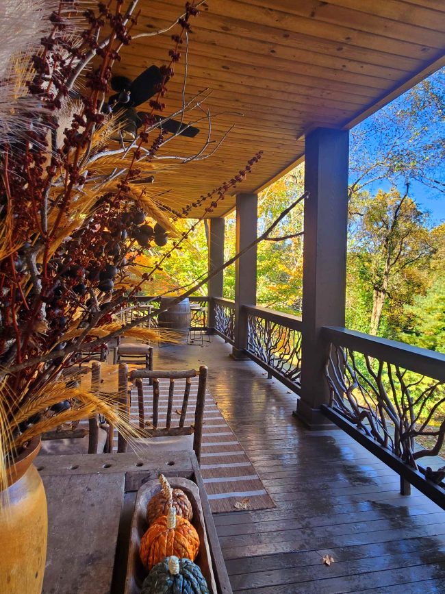 North Georgia fall getaway - Wooden porch with a trough of orange pumpkins and dried grasses, set against autumn foliage and a blue sky.