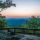 Sunset over layered blue mountain ridges viewed from a rocky overlook with a wooden railing.