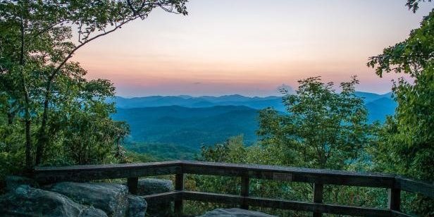 Black Rock Mountain Overlook Sunset over layered blue mountain ridges viewed from a rocky overlook with a wooden railing.