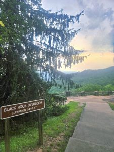 Sign reads: Black Rock Overlook, Elevation 3446 ft, with wooden railing and stair path overlooking a green valley and distant hills at sunset or dusk.
