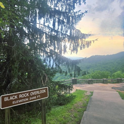 Sign reads: Black Rock Overlook, Elevation 3446 ft, with wooden railing and stair path overlooking a green valley and distant hills at sunset or dusk.