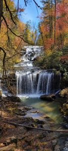 Autumn forest frames a multi-tiered waterfall cascading into a calm pool surrounded by colorful fall foliage