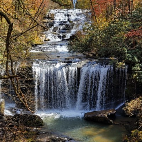 Autumn forest frames a multi-tiered waterfall cascading into a calm pool surrounded by colorful fall foliage