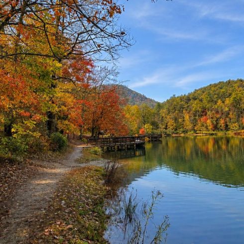 Autumn lakeside scene with colorful fall foliage along a calm lake and a wooden boardwalk stretching into the distance under a blue sky