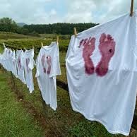 White sheets on a clothesline in a grassy field, each stamped with pink footprints.