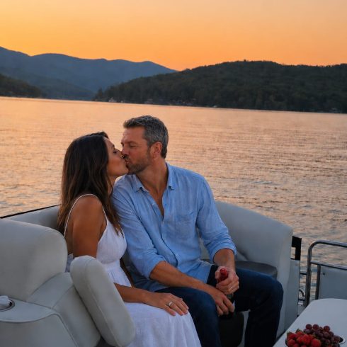 Couple kissing on a boat at sunset, with a lake and forested hills in the background.