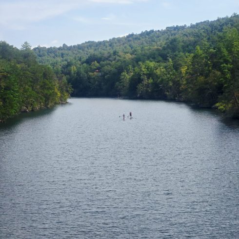 Calm lake surrounded by forested hills with two people stand-up paddleboarding in the center.