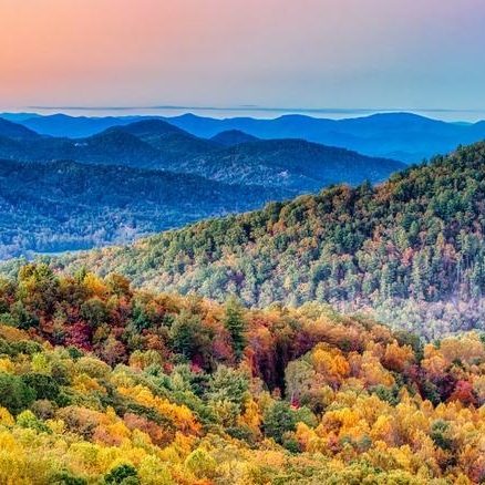 Fall foliage blankets rolling mountains under a pastel sunset sky.