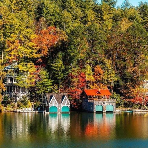 Autumn lakeside scene with colorful trees and two boathouses on a calm lake.